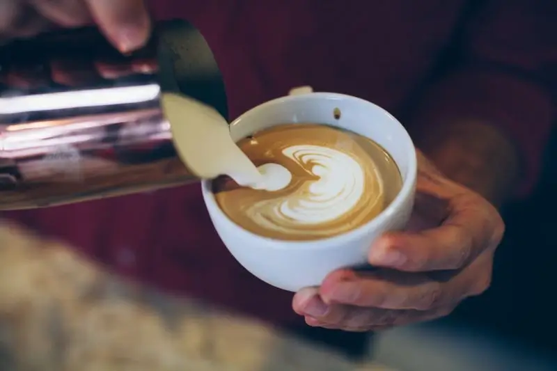 A barista pouring a latte art heart into a cup.